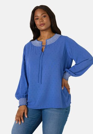 Blå bluse med tekstureret stof, prydet med en dekorativ hvid broderet krave, nøglehulåbning og elastiske manchetter. Bæret med denim jeans.