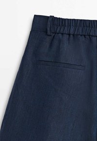 Partie de pantalon bleu foncé montrant une ceinture élastique avec passants de ceinture et une poche passepoilée horizontale à l'arrière.