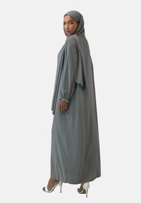 Grå hijab med matchende lang kjole med lange ærmer, samlede manchetter og flagrende stof, båret med strappy hvide hæle.