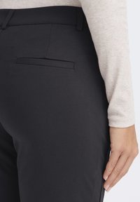 Černé přiléhavé kalhoty s hladkou texturou, s zadní kapsou a středně vysokým pasem. Boční pohled ukazuje elegantní design.