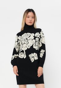 Melna turtlenecks kleita ar lielu, pelēkbalto ziedu rakstu. Adīta materiāla ar garām piedurknēm un ribotu apkakli un aprocēm.