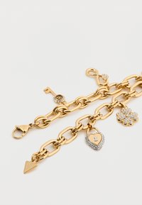 Βραχιόλι αλυσίδας σε χρυσή απόχρωση με φυλακτά: κλειδί, καρδιά με λουκέτο και στρας, σχέδιο λουλουδιού και σύμβολο απειροσύνης. Υφή στους κρίκους και κούμπωμα τύπου αστακού.