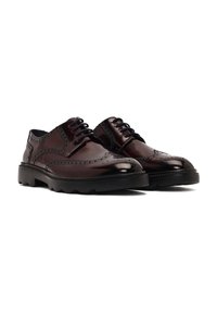 Zapatos de charol marrón con un diseño de brogue, que presentan intrincadas perforaciones y cordones negros, sobre una suela negra texturizada.