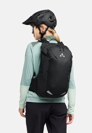 Zaino nero con spallacci regolabili, realizzato in materiale testurizzato, presenta accentuazioni riflettenti e un design elegante e curvo. Indossato con un top verde menta.