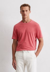Short-sleeve crew neck t-shirt in coral cotton. Features a relaxed fit and smooth texture. Paired with white trousers.