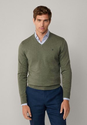 Olive green v-neck sweater in a soft knit, featuring long sleeves and a fitted waist. Simple design with a subtle logo on the chest.