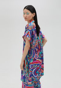 Túnica oversized colorida y estampada en púrpura, rosa y turquesa. Presenta mangas cortas y un diseño holgado y fluido.