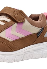 Braune Wildleder-Sportschuh mit pinkem Zickzackmuster, beigen Akzenten, Klettverschluss und einer strukturierten weißen Sohle mit einem markanten Profilmuster.
