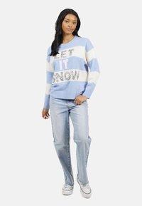 Blauw-wit gestreepte trui met de tekst "LET IT SNOW" in glinsterende accenten. Gecombineerd met lichtblauwe jeans en witte sneakers.