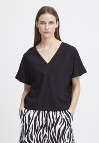 Top in lino nero con scollatura a V e maniche corte, abbinato a pantaloni a strisce zebrate bianchi e neri. Il tessuto presenta una finitura leggermente testurizzata.