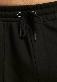 Black sweatpants featuring a drawstring waistband with black aglets and elastic around the waist, made of soft, textured fabric.