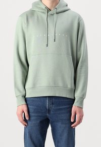 Světlé zelená mikina s kapucí a nastavitelnými šňůrkami, přední kapsa a bílé logo s textem. Vyrobena z měkkého materiálu s žebernými manžetami a lemem.