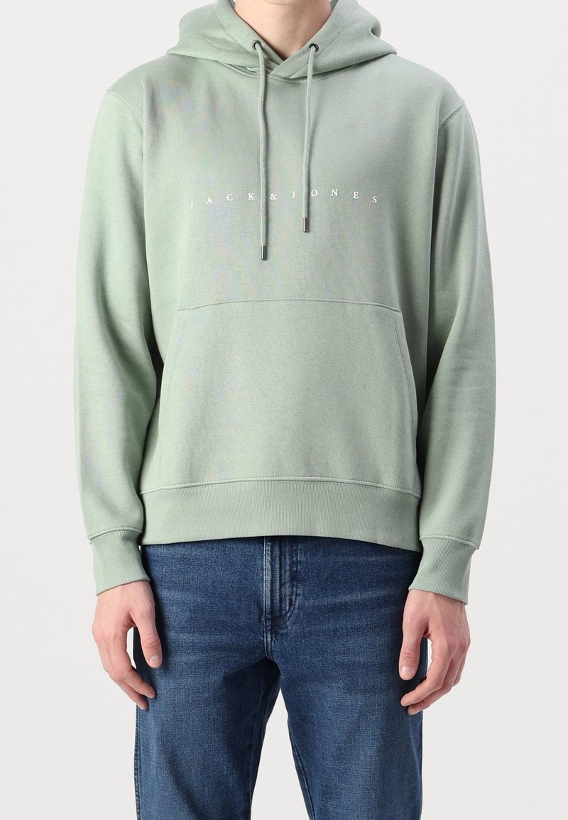 Světlé zelená mikina s kapucí a nastavitelnými šňůrkami, přední kapsa a bílé logo s textem. Vyrobena z měkkého materiálu s žebernými manžetami a lemem.