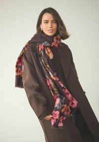 Blomstret tørklæde med en mørk burgunder baggrund og livlige pink, blå og grønne blomster. Blødt stof med frynset kanter og letvægtsdesign.