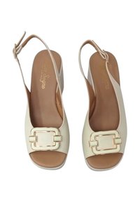 Scarpe beige open-toe slingback con tacco spesso, caratterizzate da un accento in metallo dorato e una texture in pelle liscia.