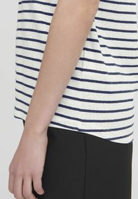Top a maniche corte a righe con righe orizzontali blu navy e bianche, realizzato in tessuto morbido, con un fit rilassato e spacco laterale. Pantaloni neri.