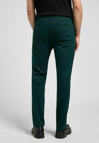 Grüne Hosen aus glattem Stoff, mit Gesäßtaschen und geradem Bein, kombiniert mit schwarzen Schuhen.