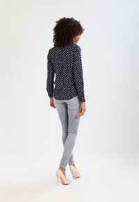 Blusa a maniche lunghe blu navy con un piccolo motivo floreale rosa e bianco, abbinata a jeans skinny grigi chiari e tacchi nudi.