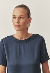 Navyblaues Kurzarmbluse mit Rundhalsausschnitt aus einem glatten Stoff. Hervorzuheben sind das schlichte Design und der lockere Schnitt.