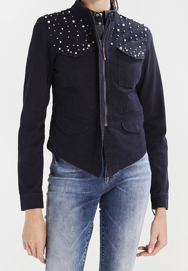 Marinblå jacka med nitar på axlarna, framzip och två bröstfickor, med en strukturerad design och texturerad tyg.