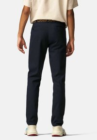 Navyblauwe chinos met een slim fit, voorzien van een geweven meerkleurige riem en achterzakken, gedragen met lichtgekleurde sneakers.