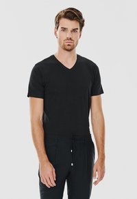 Czarny T-shirt z krótkim rękawem i dekoltem w serek, dopasowany krój, gładka tekstura. Model nosi czarne spodnie z detalem na sznurku, stoi na tle białym.