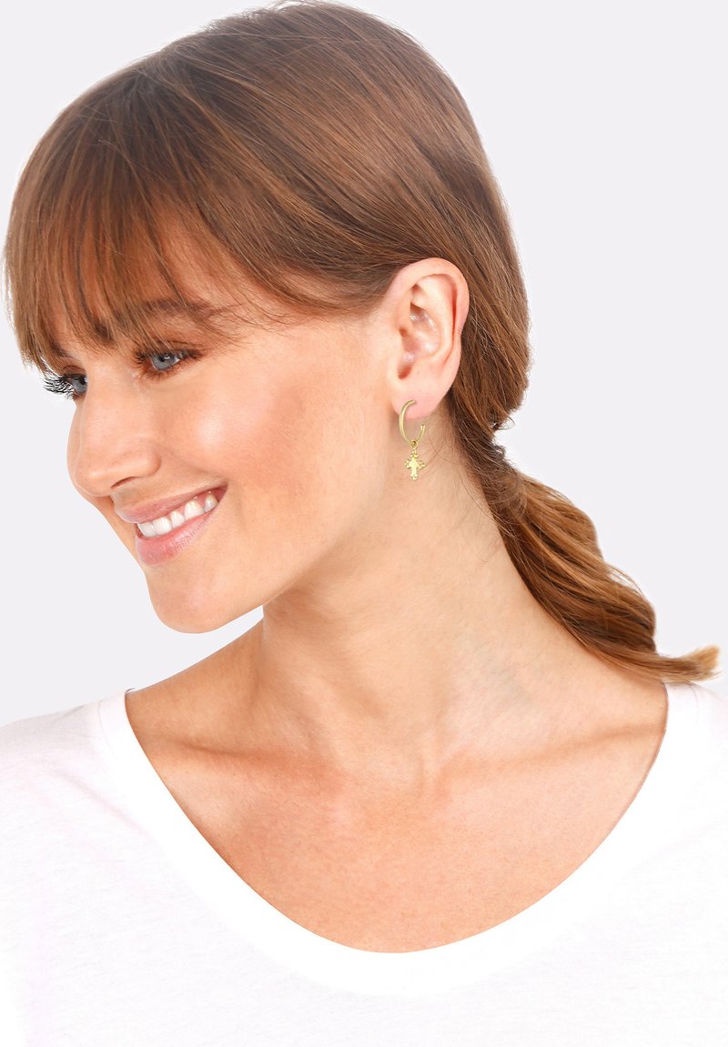 Des boucles d'oreilles en or en forme de créoles présentent un petit charme en forme d'étoile, suspendu à la créole. Le design est délicat et léger.