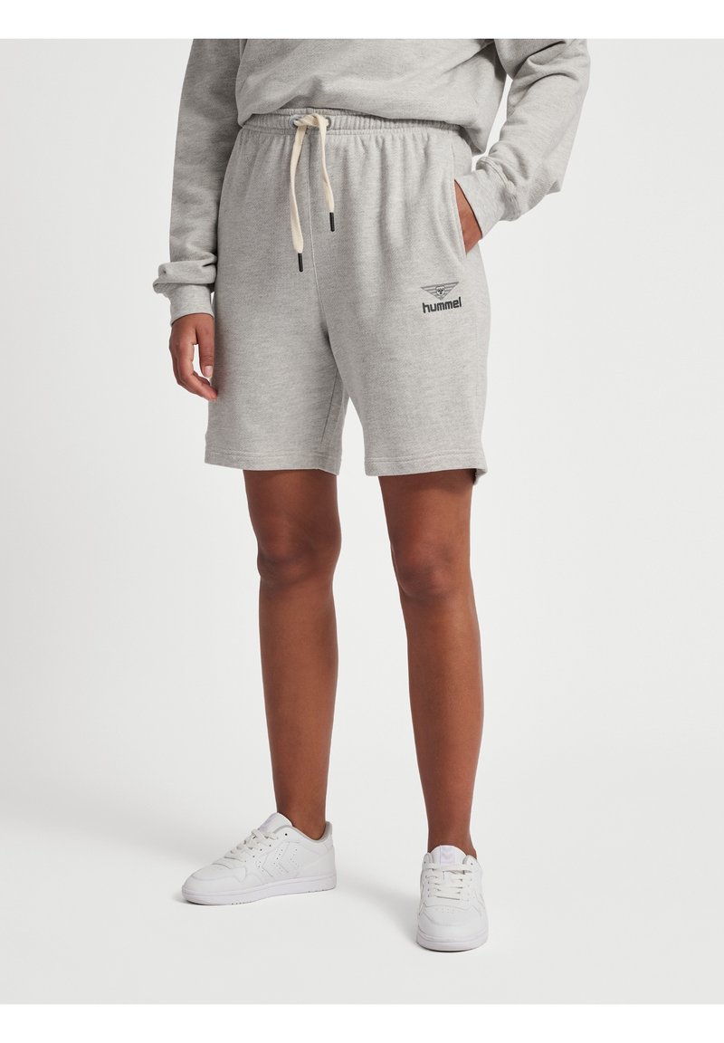 Personne portant un short hummel gris clair avec cordon, un sweat assorti et des baskets blanches, debout devant un fond uni.