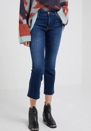 Kobieta ubrana w ciemnoniebieskie krótkie dżinsy z surowymi brzegami, wielokolorowy, oversize sweter oraz czarne botki na słupku.