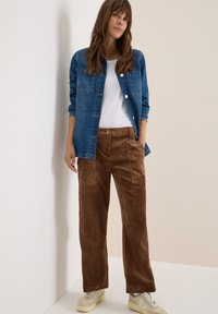 Blauwe spijkerblouse over een wit T-shirt, gecombineerd met bruine corduroy broek. Neutrale sneakers maken de outfit compleet. Eenvoudig, casual ontwerp.