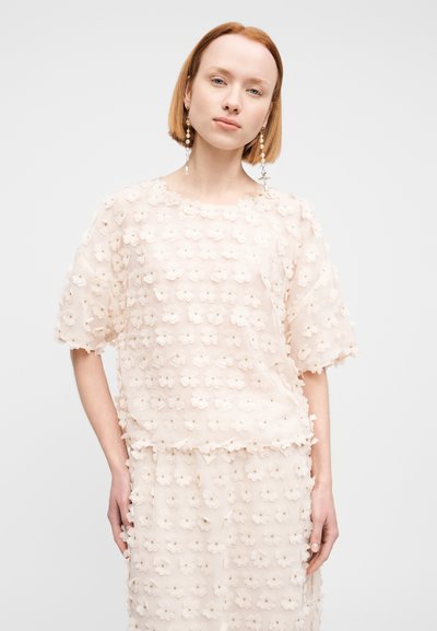 Haut à application florale en rose clair, tissu transparent avec un col rond et des manches courtes. Présente des détails de fleurs 3D texturées sur toute la surface.
