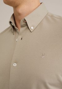 Beige Poloshirt aus strukturiertem Stoff. Verfügt über einen klassischen Kragen, drei Knöpfe und ein dezent gesticktes Logo auf der Brust.