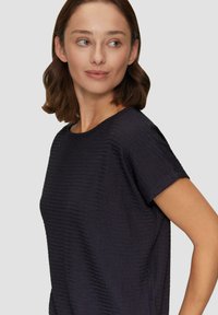 Granatowa bluzka z krótkim rękawem, z teksturowanym, prążkowanym wzorem; okrągły dekolt i luźny krój.