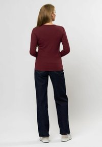 Bluză burgundă cu mânecă lungă, cu o textură canelată, asortată cu blugi largi de culoare albastră închis și adidași de culoare deschisă.