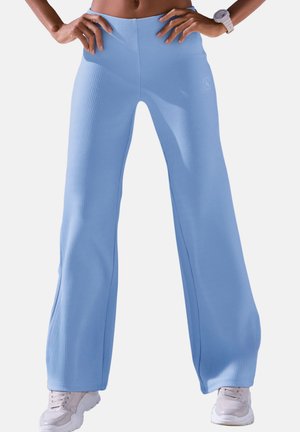 Hellblaue, gerippte Schlaghosen mit hohem Bund und seitlichen Schlitzen, kombiniert mit hellfarbenen Sportschuhen.