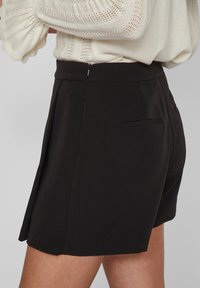 Svarta skräddarsydda shorts i ett glatt tyg, med en sidodragkedja och en bakficka, stylade med veck för ökad struktur.