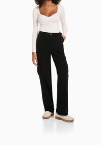 Musta cargo-housut, joissa sivutaskut ja suorat lahkeet, yhdistettynä valkoiseen ribbineulottuun pitkähihnaiseen paitaan ja valkoisiin lenkkareihin, joissa on vaalea pohja.