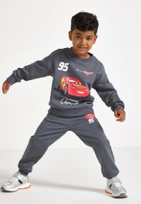 Harmaa huppari ja siihen sopivat verkkahousut, joissa on kirkkaan punainen Lightning McQueen -grafiikka, kontrastoivalla valkoisella tekstillä ja urheilullisella muotoilulla.