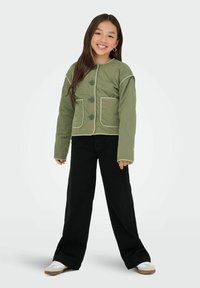 Grön quiltad jacka med rund krage, tre stora svarta knappar och två framfickor. Matchas med svarta vida byxor och vita skor.