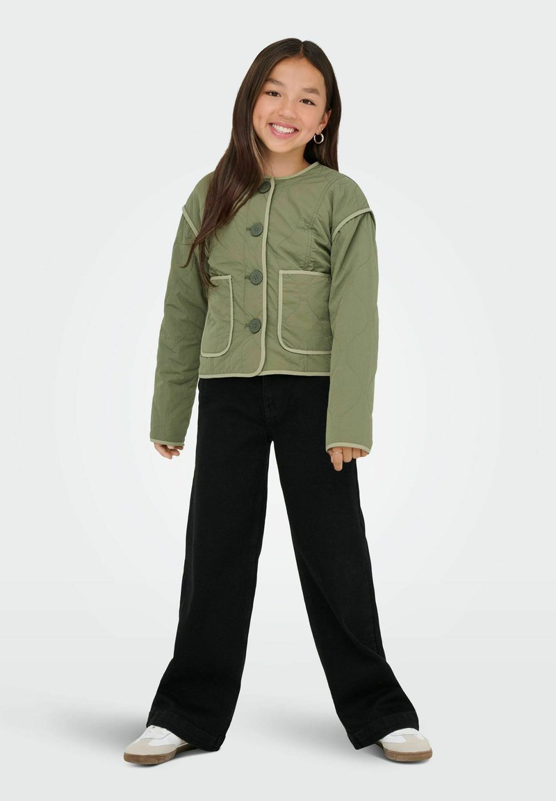 Grön quiltad jacka med rund krage, tre stora svarta knappar och två framfickor. Matchas med svarta vida byxor och vita skor.