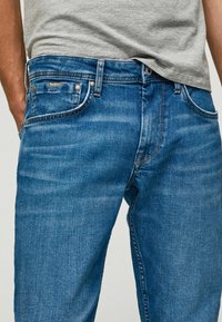 Blå denimjeans med rak passform, fem fickor, subtila slitningar och silverfärgad knappstängning. Märke på bakre midjebandet.