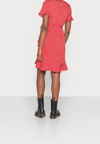 Vestido rojo con lunares blancos, mangas cortas con volantes, estilo cruzado y dobladillo acampanado. Combinado con botines negros hasta el tobillo.