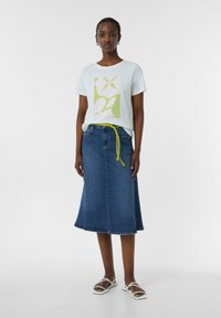 T-shirt en coton bleu clair avec un graphique floral vert et blanc, associé à une jupe trapèze en denim foncé et une ceinture jaune vif.