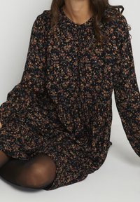 Robe noire à motifs floraux avec manches longues, ornée de fleurs multicolores et à la coupe décontractée. Tissu doux et léger, détail de boutons au niveau du col.