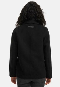 Černý vlněný kabát s klopovým límcem, se hladkým povrchem a minimalistickým designem. Na horní části zad je umístěná visačka s logem.