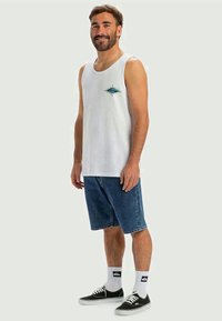 White cotton tank top with an embroidered blue and green design, paired with blue denim shorts and black sneakers.