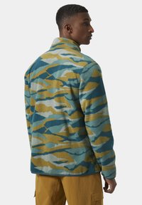 Chaqueta de forro polar en un patrón de camuflaje azul, verde azulado y amarillo. Presenta un cuello alto y un corte relajado. Textura suave con bolsillos laterales.