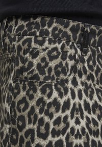 Zone de poche d'un jean en denim à motif léopard avec une passants de ceinture noire et une partie d'un haut noir visible.