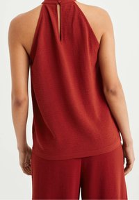 Vinröd ärmlös topp med texturerad yta, nyckelhålsöppning i ryggen och en lös passform, som matchas med lösa byxor.