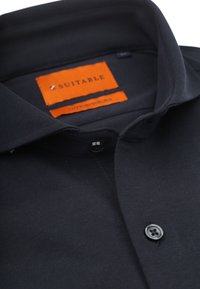 Zwarte katoenen/sorona shirt met een klassieke kraag, enkele zwarte knop en een oranje label met de tekst "SUITABLE." Gladde textuur en gestroomlijnd ontwerp.